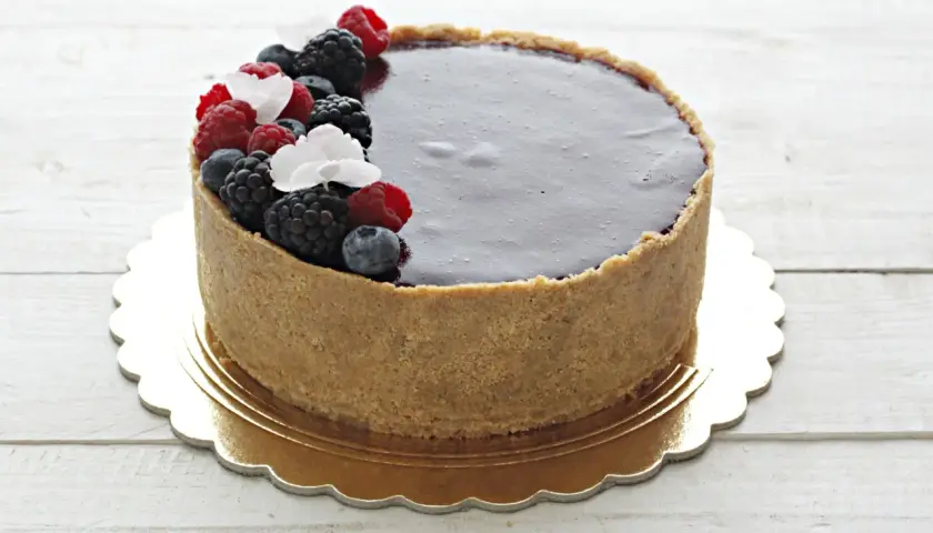 Delizioso cheesecake ai frutti di bosco con copertura al cioccolato fondente, decorato con lamponi, mirtilli e more freschi.