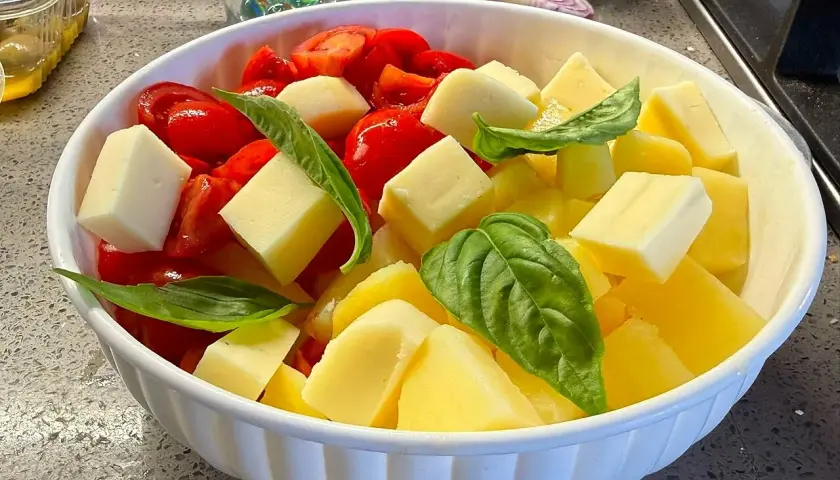 Insalata di pomodori freschi, cubetti di formaggio e foglie di basilico in una ciotola bianca.