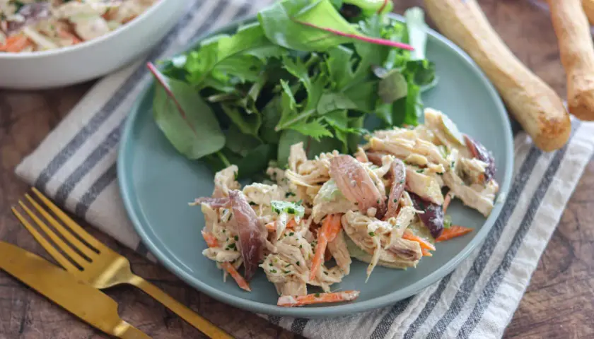 Deliziosa insalata di pollo con carote, sedano e un tocco di erbe fresche, servita con un contorno di insalata mista.