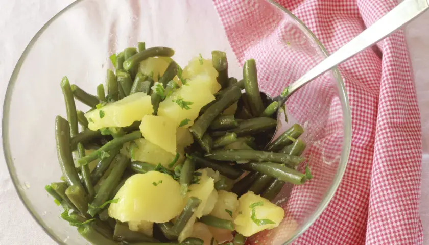 Insalata di fagiolini e patate, condita con erbe fresche, servita in una ciotola di vetro su un tovagliolo a quadretti rossi.