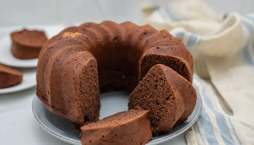 Un delizioso ciambellone al cioccolato, soffice e invitante, con una fetta tagliata che mostra la sua morbidezza.