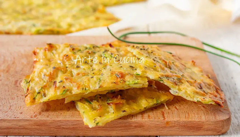 Schiacciata di zucchine dorata e croccante, condita con erbe aromatiche, servita su un tagliere di legno.