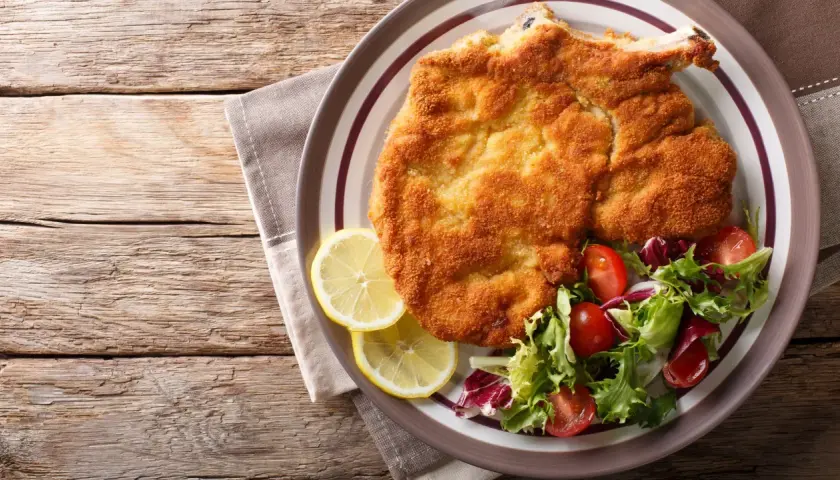 Una dorata cotoletta alla milanese, croccante e succulenta, servita con spicchi di limone e un'insalata fresca.