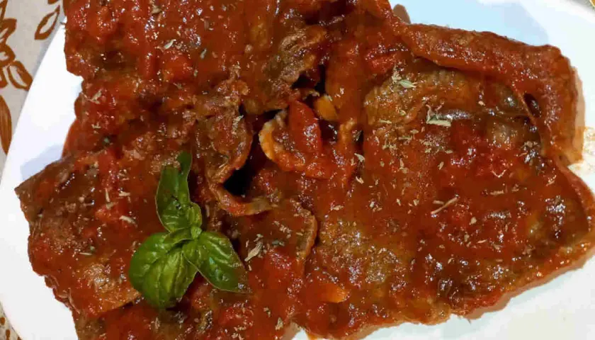 Fette di carne alla pizzaiola siciliana, ricoperte da un sugo rosso saporito e guarnite con basilico fresco.