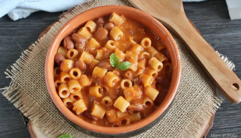 Un piatto fumante di pasta e fagioli in scatola, guarnito con menta fresca, servito in una ciotola di terracotta su una tovaglietta di juta.