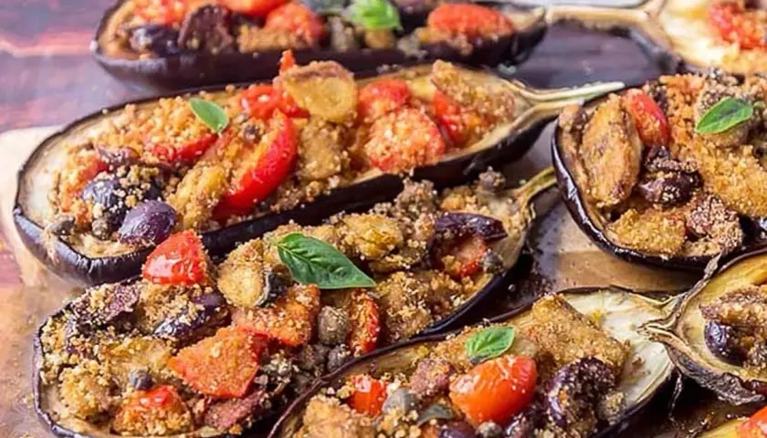 Melanzane a scarpone ripiene di pomodorini, olive e pangrattato, guarnite con basilico fresco. Un piatto saporito e invitante.