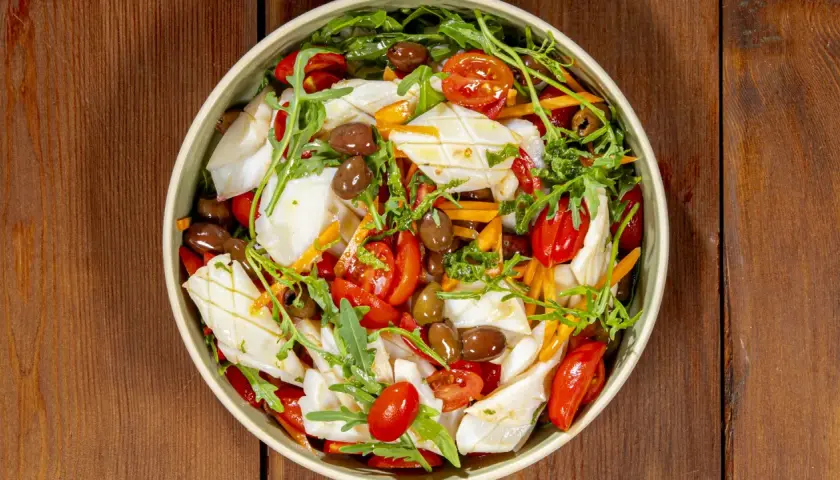 Insalata di calamari fresca con pomodorini, olive, rucola e carote julienne, un piatto estivo colorato e saporito.