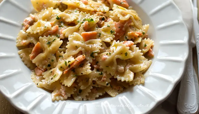 Farfalle cremose con salmone affumicato, un piatto delizioso e invitante, guarnito con prezzemolo fresco e pepe nero.