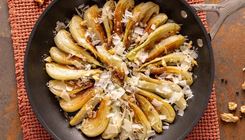 Finocchi in padella dorati, guarniti con scaglie di formaggio e noci croccanti. Un piatto semplice e saporito.