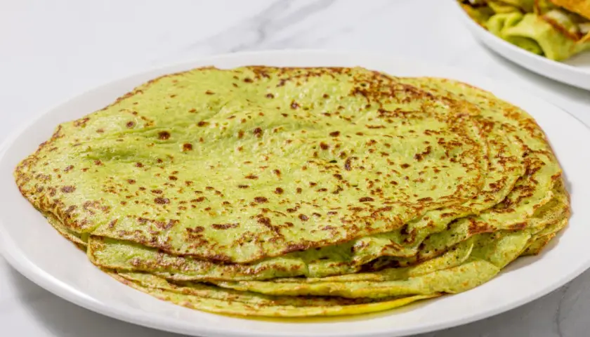 Piatto di crepes di zucchine verdi, sottili e leggermente dorate, impilate su un piatto bianco.
