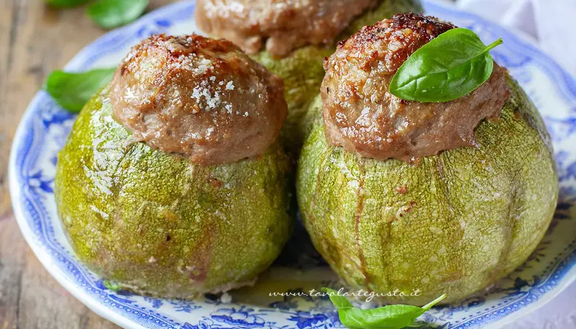 Zucchine tonde ripiene, un piatto gustoso e colorato, guarnito con basilico fresco e parmigiano.