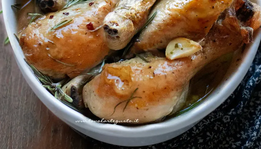 Cosce di pollo al forno succulente, dorate e profumate al rosmarino e aglio, servite in una ciotola bianca.