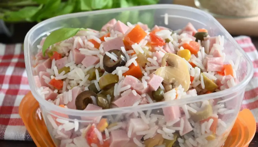 Insalata di riso colorata con prosciutto a cubetti, carote, olive, piselli e funghi, pronta per un pasto veloce.