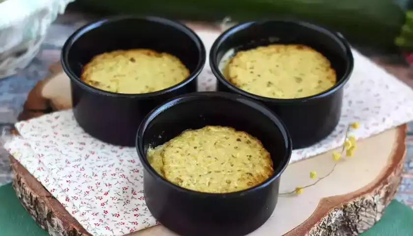 Tre deliziosi flan di zucchine appena sfornati in stampini neri, pronti per essere gustati.