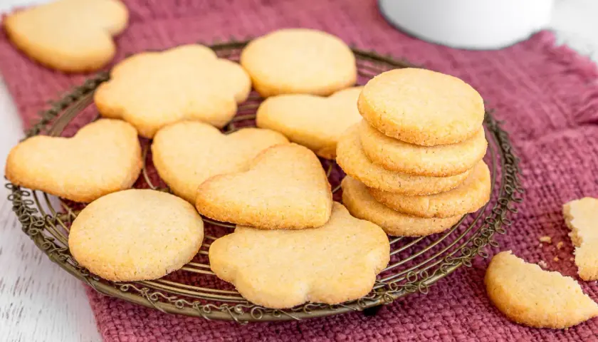 Deliziosi dolci da fare in casa: biscotti a forma di cuore e fiori su una gratella, con una pila di biscotti rotondi e un pezzo rotto in primo piano.