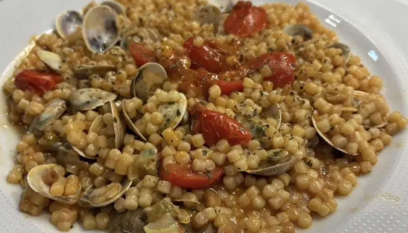 Un piatto invitante di fregola con vongole, pomodorini e prezzemolo, pronto per essere gustato.