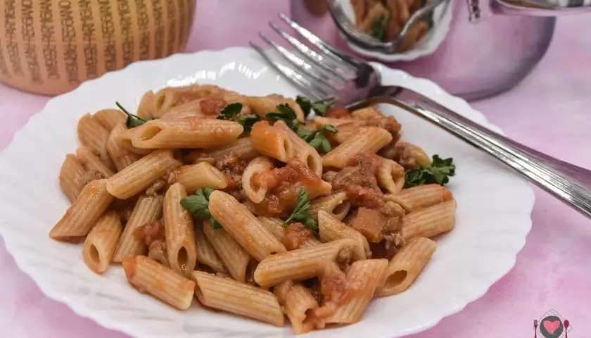 Piatto di pasta con salsiccia e pomodoro, guarnito con prezzemolo fresco. Un classico della cucina italiana, pronto per essere gustato.