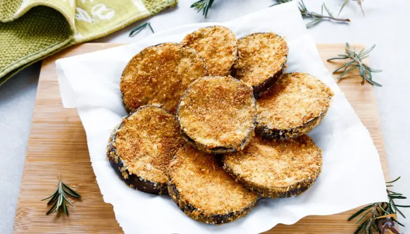 Cotolette di melanzane dorate e croccanti, servite su carta bianca con rametti di rosmarino.