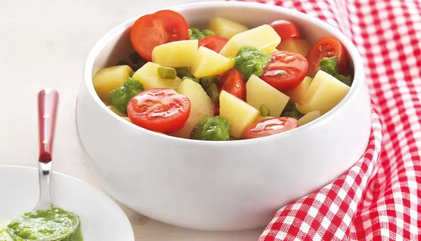 Deliziosa insalata di patate estiva con pomodorini e piselli, condita con un pesto fresco. Perfetta per un picnic o una cena leggera.