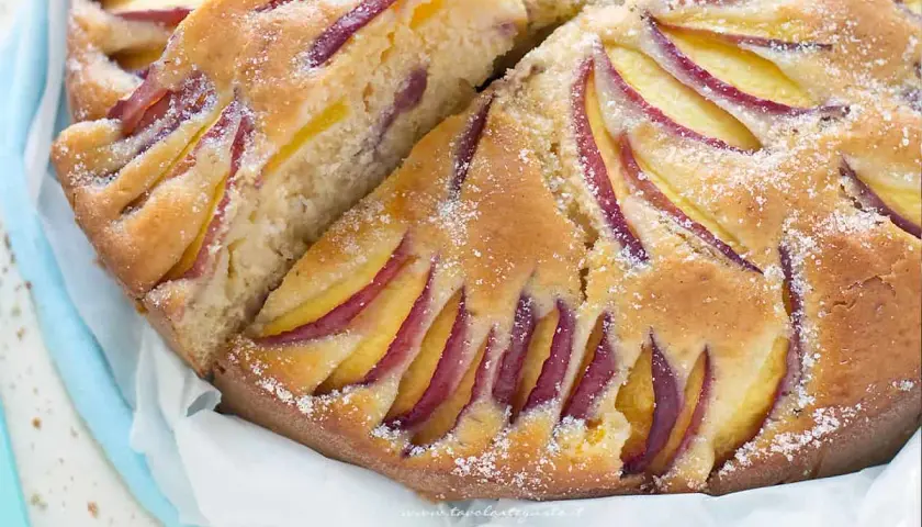 Una deliziosa torta di pesche, con fette di frutta disposte a raggiera sulla superficie dorata e cosparsa di zucchero.