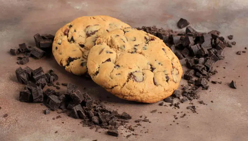 Due golosi cookies con gocce di cioccolato, perfetti per la tua ricetta crumble cookies, circondati da pezzetti di cioccolato fondente.
