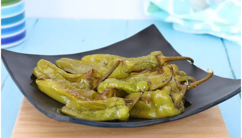 Friggitelli al forno, verdi e lucidi, serviti su un piatto nero. Un contorno saporito e facile da preparare.