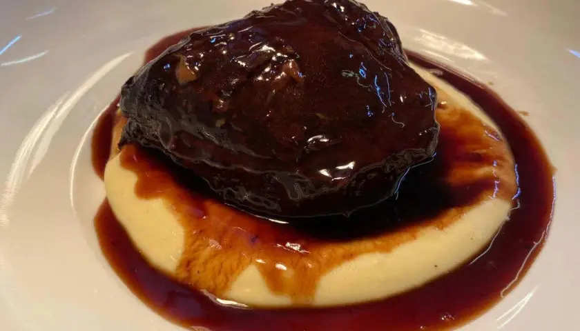 Guancia di manzo brasata, tenerissima e succulenta, adagiata su un letto di purè cremoso, il tutto avvolto da una ricca salsa scura.