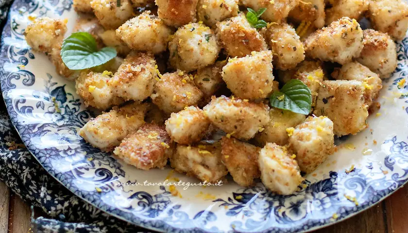 Croccante spezzatino di pollo impanato, guarnito con scorza di limone e menta fresca, servito su un piatto decorato.