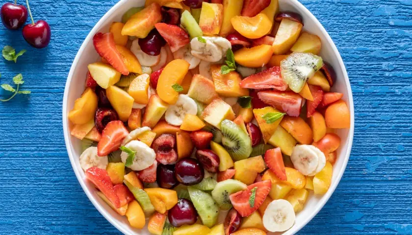 Una colorata macedonia di frutta fresca, con fragole, kiwi, pesche, banane e ciliegie, pronta per essere gustata.