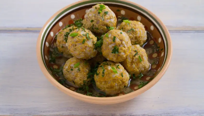 Polpette di riso avanzato, dorate e profumate, servite in una ciotola decorata, con erbe fresche tritate.