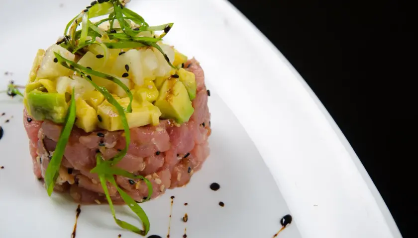 Deliziosa tartare di tonno con avocado, ananas e cipollotto fresco, guarnita con semi di sesamo e un filo di salsa.