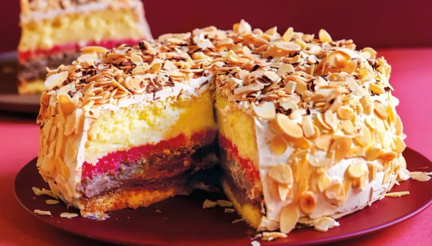 Una fetta di pizza dolce abruzzese, con strati di crema, cioccolato e confettura, ricoperta di mandorle tostate e scaglie di cioccolato.