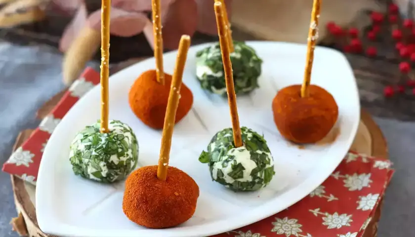 Sfere di ricotta al forno, alcune ricoperte di erbe fresche, altre di paprika, infilzate con grissini.