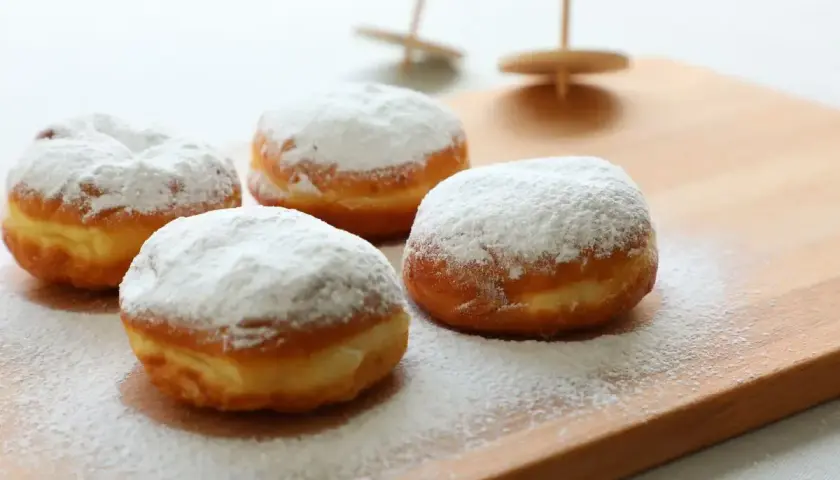 Quattro soffici bomboloni alla crema, cosparsi di zucchero a velo, invitano a un dolce momento.