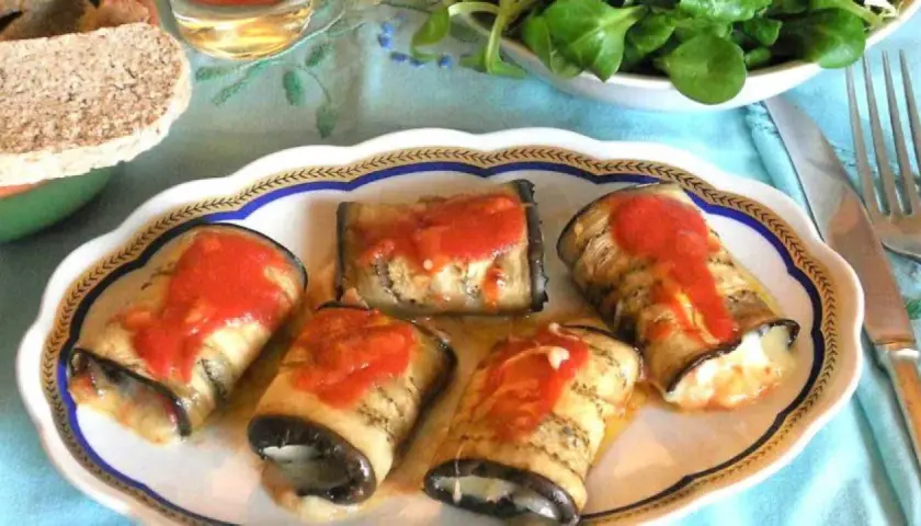 Deliziosi involtini di melanzane ripieni, conditi con sugo di pomodoro, su un piatto decorato.
