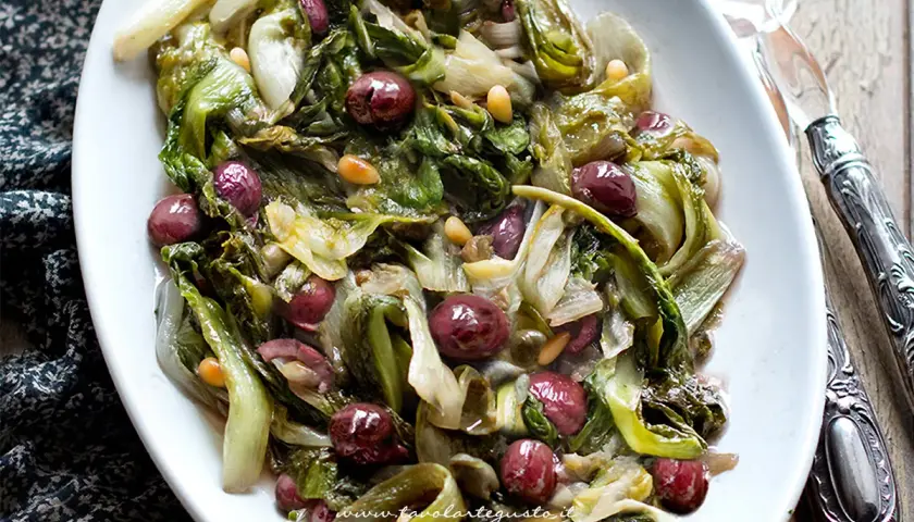 Scarola in padella con olive nere e pinoli, un contorno saporito e colorato, pronto per essere gustato.