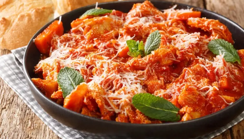 Trippa alla romana, la ricetta della nonna, servita in una ciotola scura con parmigiano e menta. Accanto, pane casereccio.