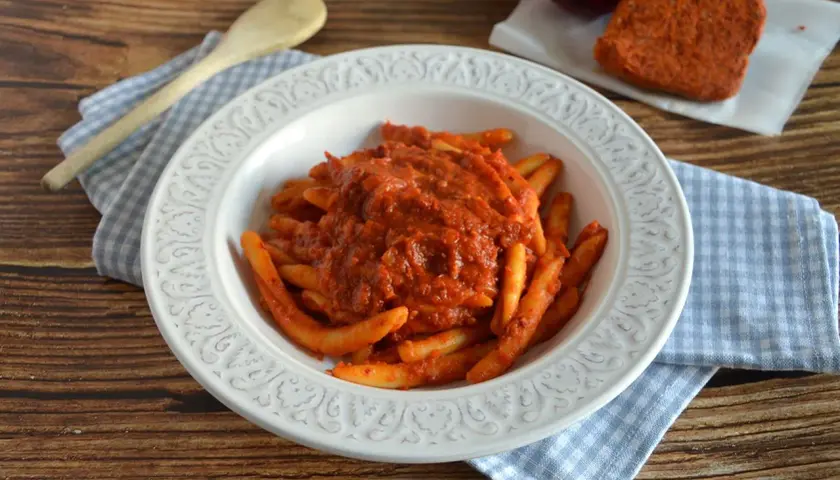 Piatto di pasta con sugo rosso piccante, condita con nduja calabrese. Accanto, un pezzo di nduja e cipolla rossa.