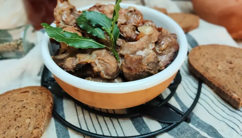 Durelli di pollo saporiti in ciotola, guarniti con foglie di alloro, accompagnati da fette di pane rustico.