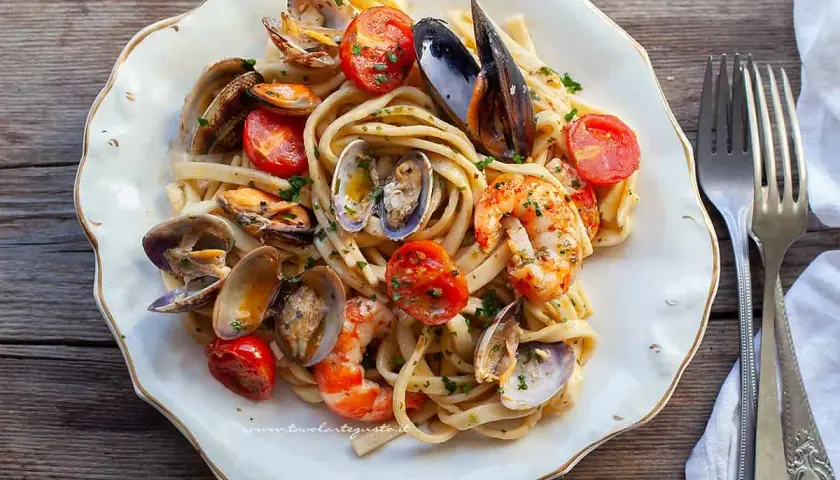 Un piatto invitante di scialatielli ai frutti di mare, con cozze, vongole e gamberi, guarnito con pomodorini e prezzemolo.