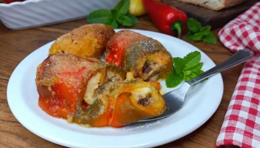 Deliziosi involtini di peperoni ripieni, dorati e succulenti, serviti su un piatto bianco con menta fresca.