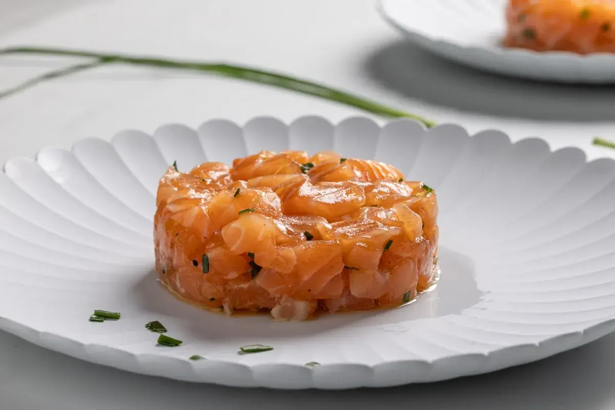 Tartare di salmone fresco, finemente tagliato e condito, servito su un piatto bianco con erba cipollina.