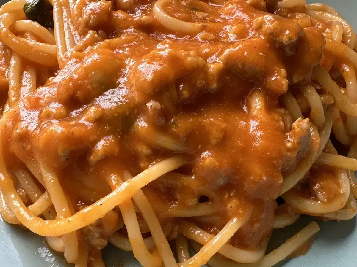 Un piatto di spaghetti al ragù, con un sugo ricco e saporito, dove spiccano i pomodorini.