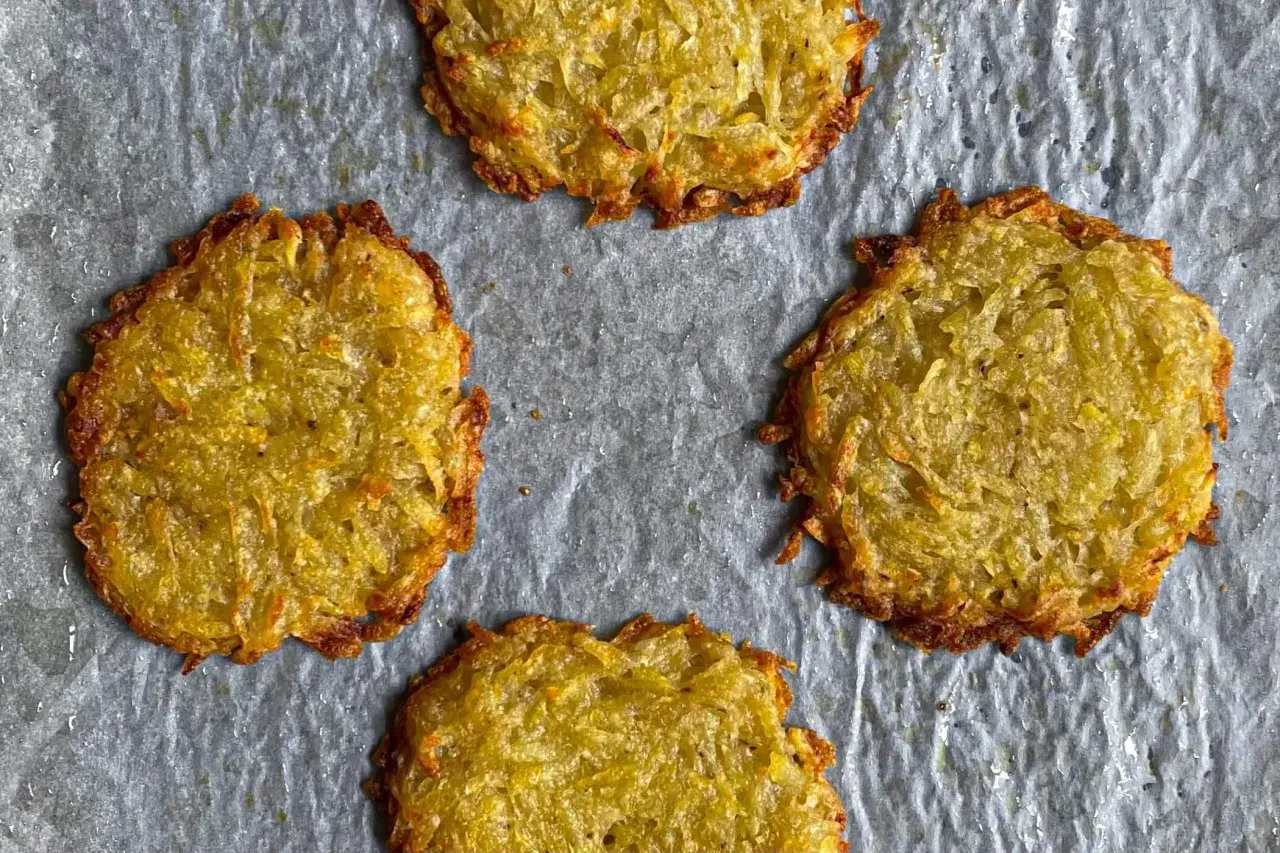 Quattro rosti di patate dorati e croccanti su carta da forno.