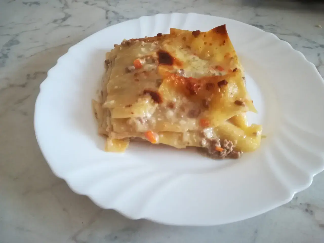 Porzione di lasagna classica, con strati di pasta, ragù e besciamella, servita su un piatto bianco.