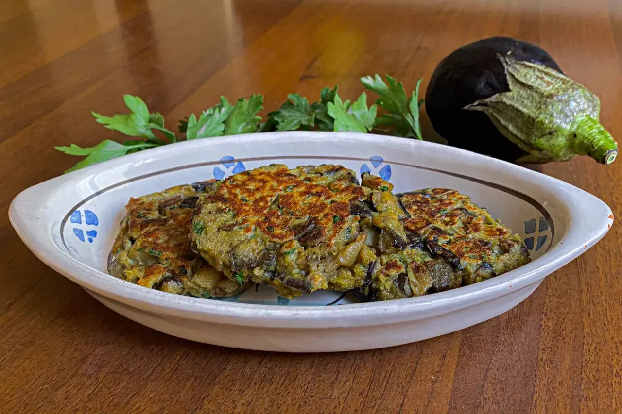 Tre hamburger di melanzane dorati e appetitosi in un piatto decorato, con un'altra melanzana e prezzemolo sullo sfondo.