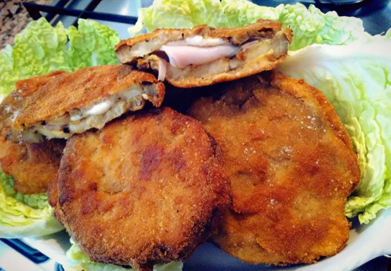 Cordon bleu di melanzane dorati e croccanti, ripieni di prosciutto e formaggio filante, serviti su un letto di lattuga fresca.