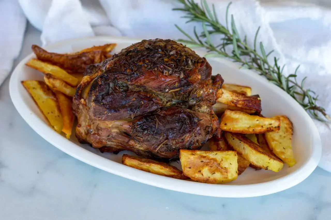 Stinco di maiale arrosto, dorato e succulento, servito con patate croccanti e rosmarino fresco.