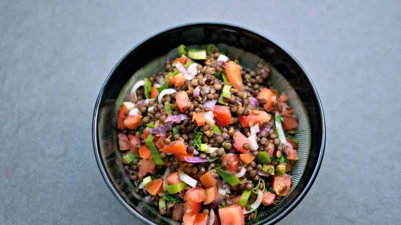 Una ciotola di insalata di lenticchie colorata con pomodori, cipolla rossa e erbe fresche.