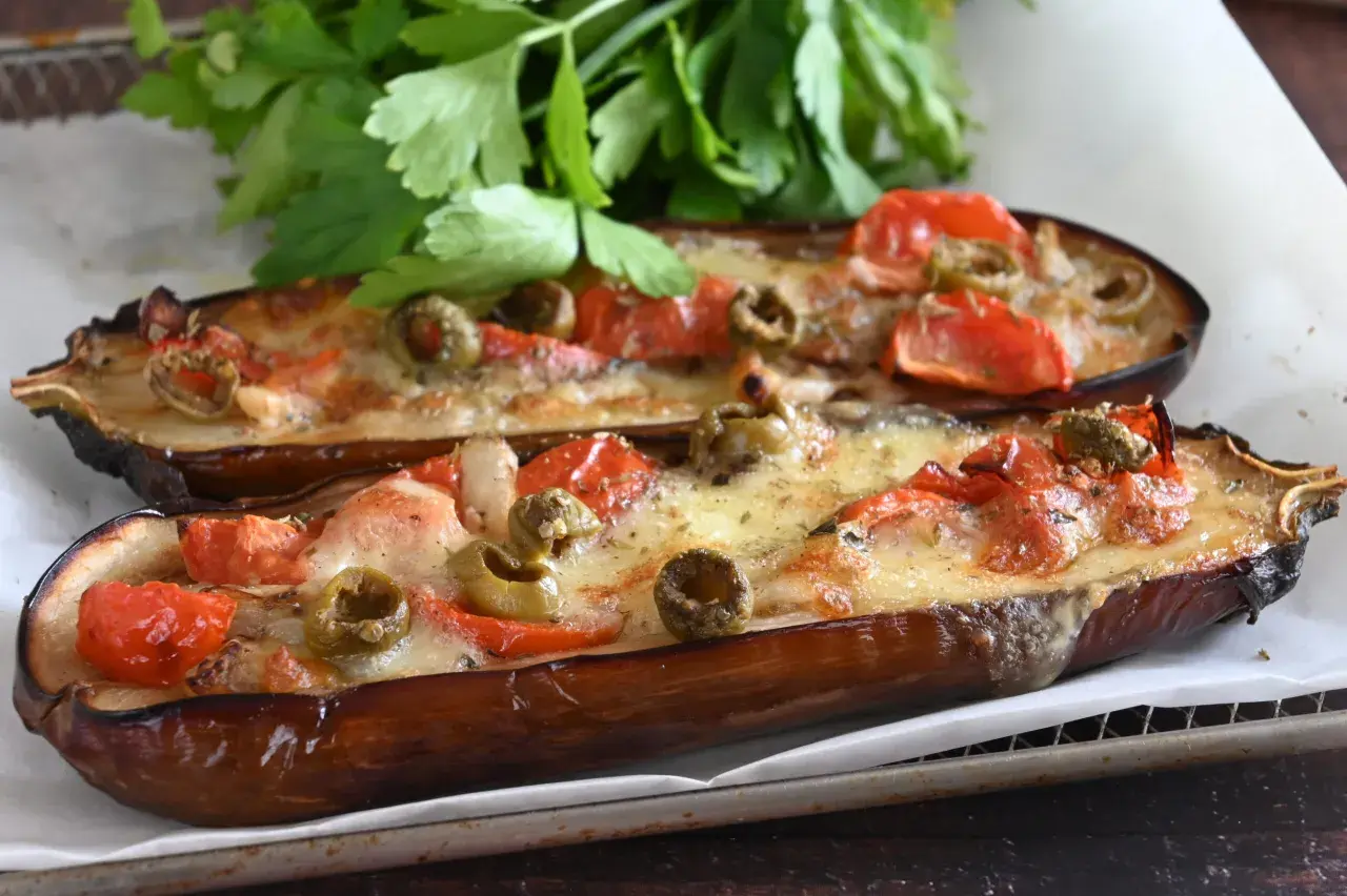 Melanzane alla pizzaiola, gustose e filanti, con pomodoro, olive e formaggio fuso, guarnite con prezzemolo fresco.